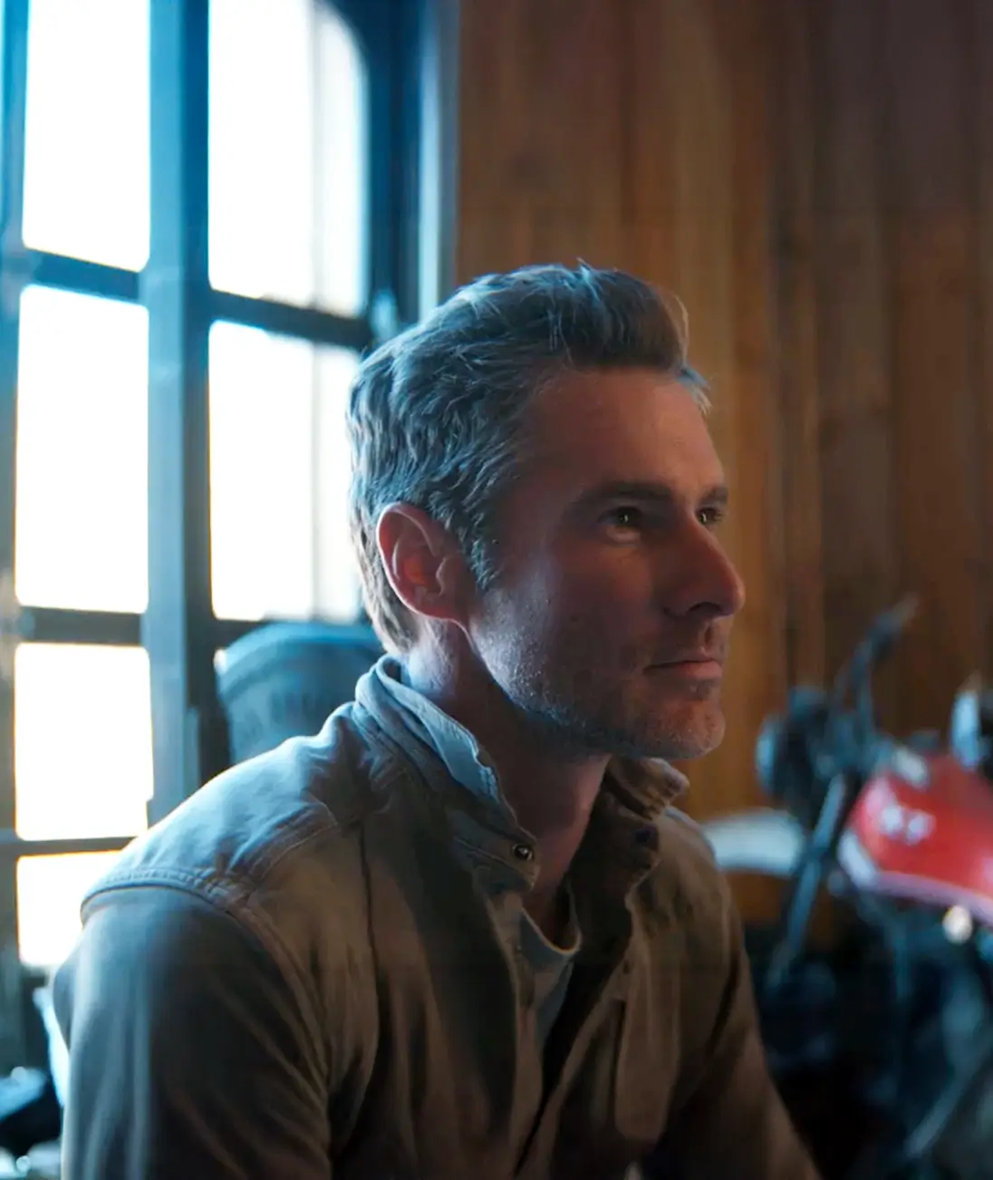 Man looking to the side in a warmly lit room with a motorcycle behind him