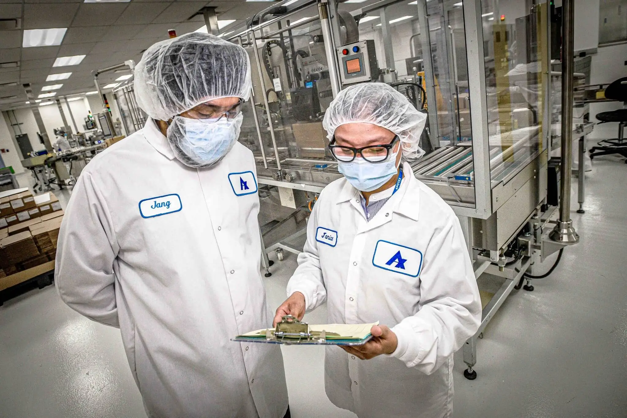 Two workers in masks and lab coats looking at a clipboard