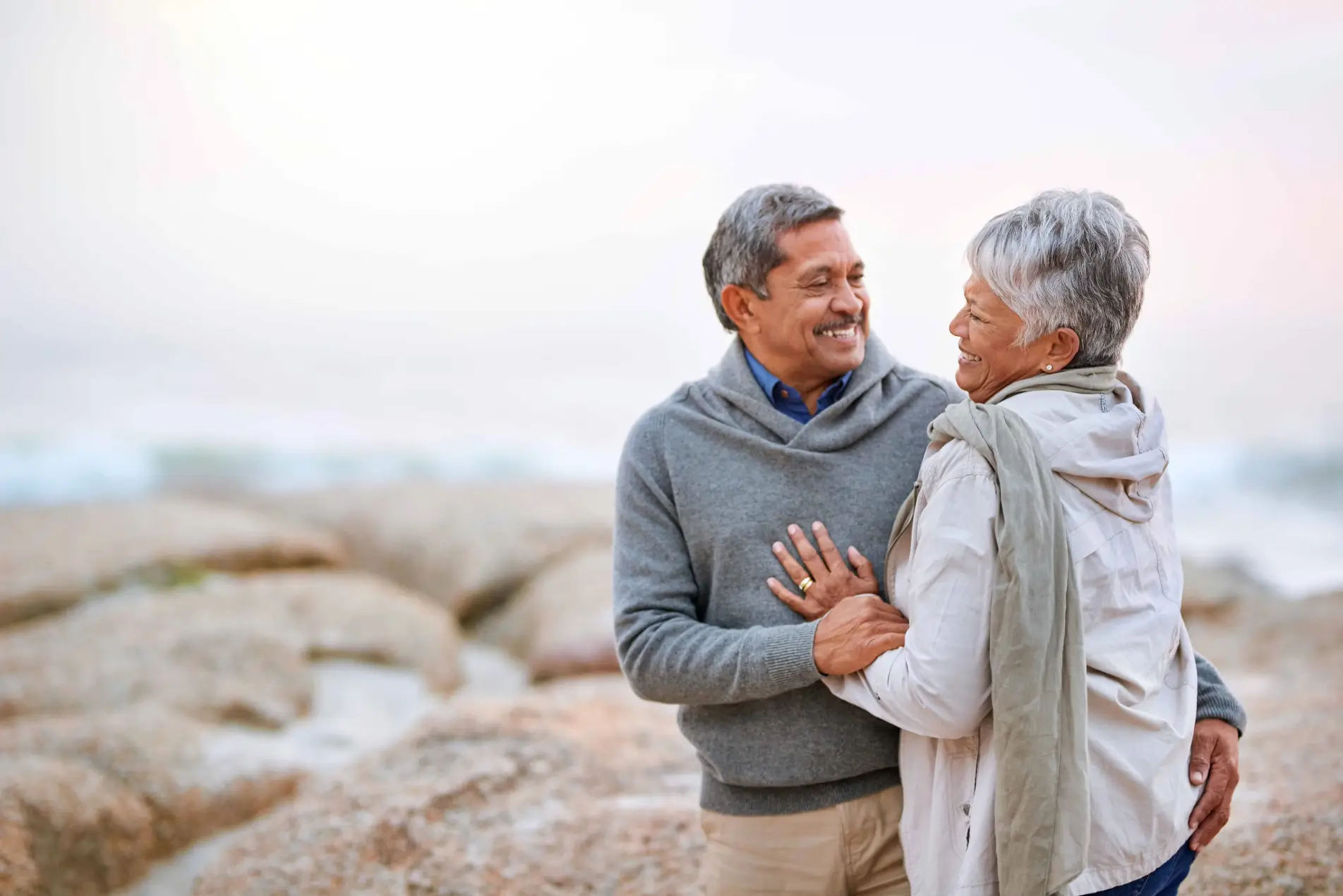 Sonriente pareja de ancianos abrazándose en una playa rocosa.