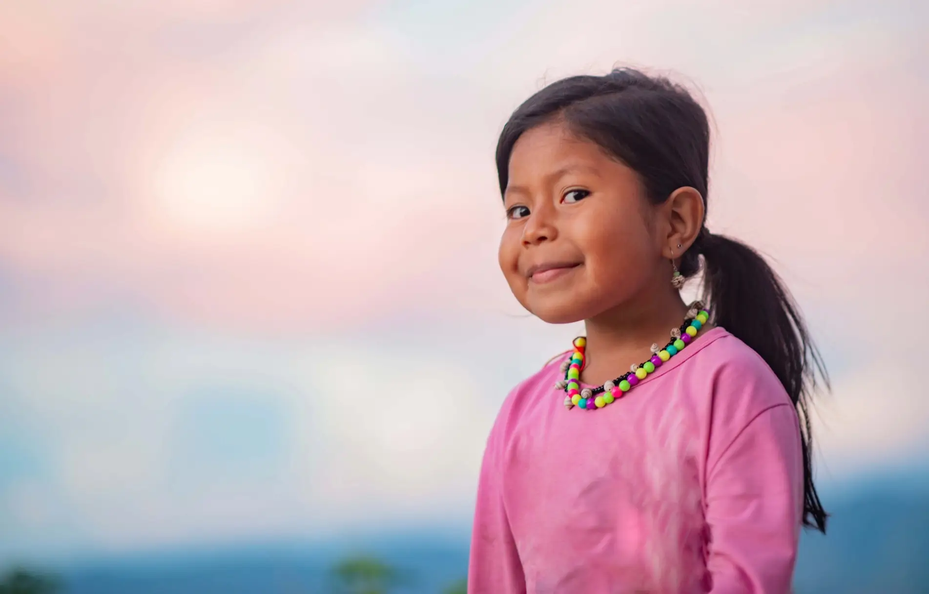 A young girl with a colorful necklace smiling at the camera.